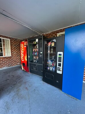 A vending machine with a Coca-Cola logo, a blue door, and a brick wall background. - Motel Jesup Near US 301 (Jesup)