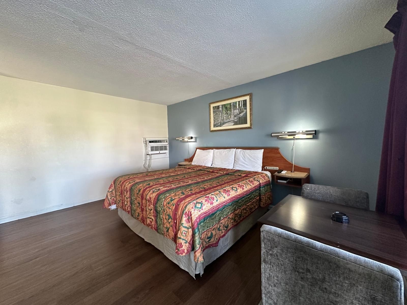 Habitación de hotel con cama, escritorio, silla, equipo de aire acondicionado y lámpara fijada a la pared.