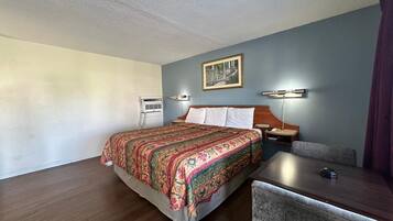 Habitación de hotel con cama, escritorio, silla, equipo de aire acondicionado y lámpara fijada a la pared.