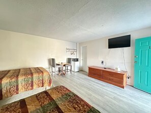 Une chambre avec deux lits, un bureau avec des chaises, une commode, un téléviseur et une porte de couleur turquoise.