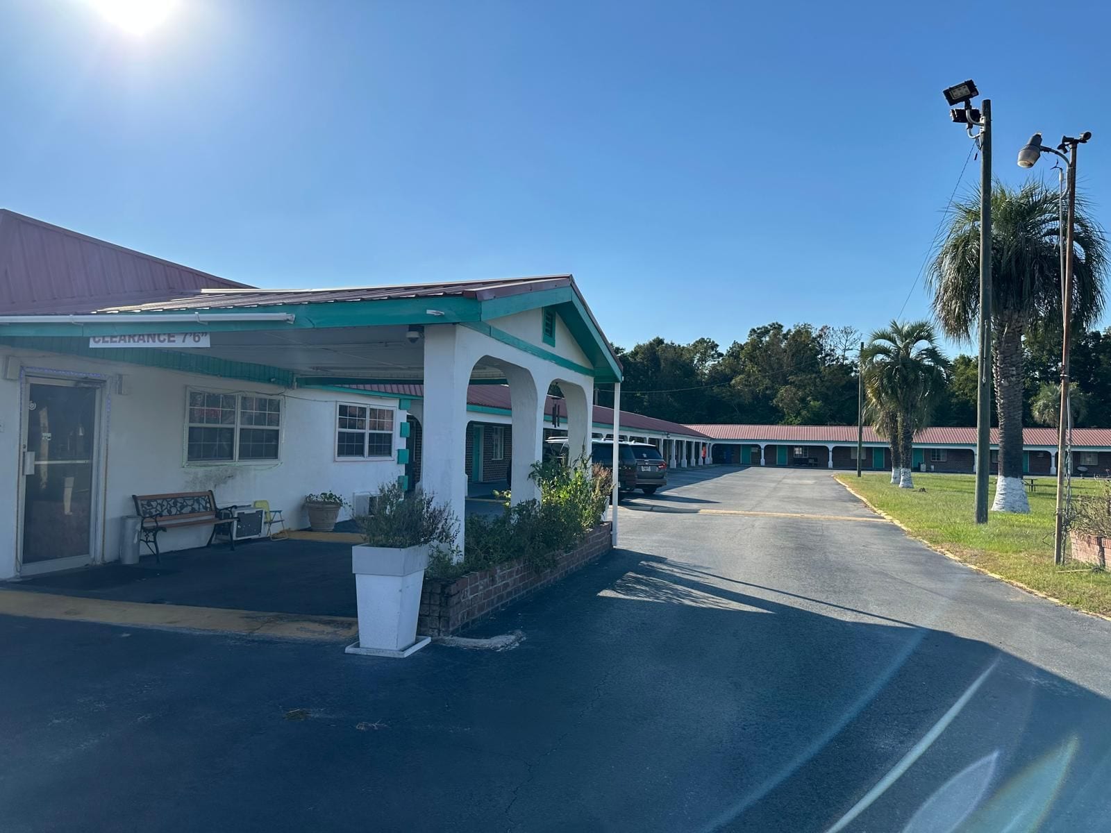 A motel with a covered parking area, a bench, and a sign indicating a clearance of 7'6'.