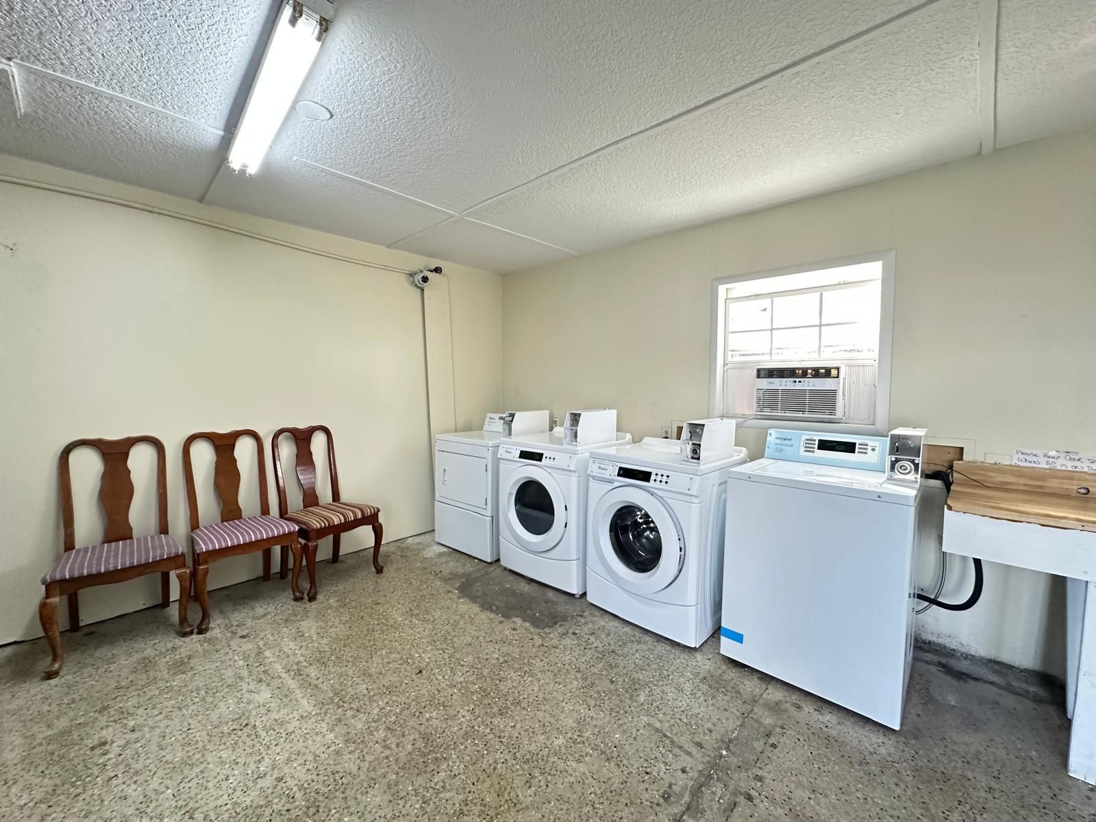 A laundry room with a washing machine, dryer, and a wooden chair.