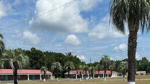 A row of single-story buildings with red roofs, surrounded by palm trees and a clear sky. - Motel Jesup (Jesup)