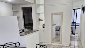 Una cocina moderna con armarios blancos, encimera negra y estufa integrada. Cuenta con un comedor con una mesa redonda y sillas negras. El suelo está cubierto de baldosas, y hay una puerta que da a un balcón.