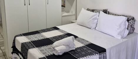 A bedroom with a bed, white curtains, a wardrobe, and a shelf with decorative items.