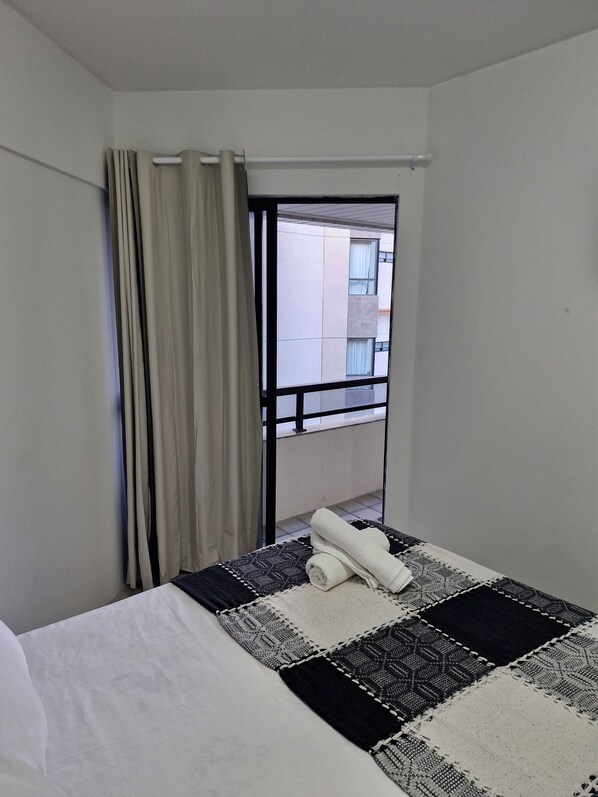 A hotel room with a bed, a window with curtains, and a view of a building outside. - Apartamento Beira Mar Praia de Pajuçara (Maceio)