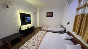 Habitación de hotel con dos camas, televisión, escritorio y ventilador de techo.
