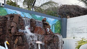 Una cascada con una estatua de cisne y una de rana, rodeada de piedras y un mural.