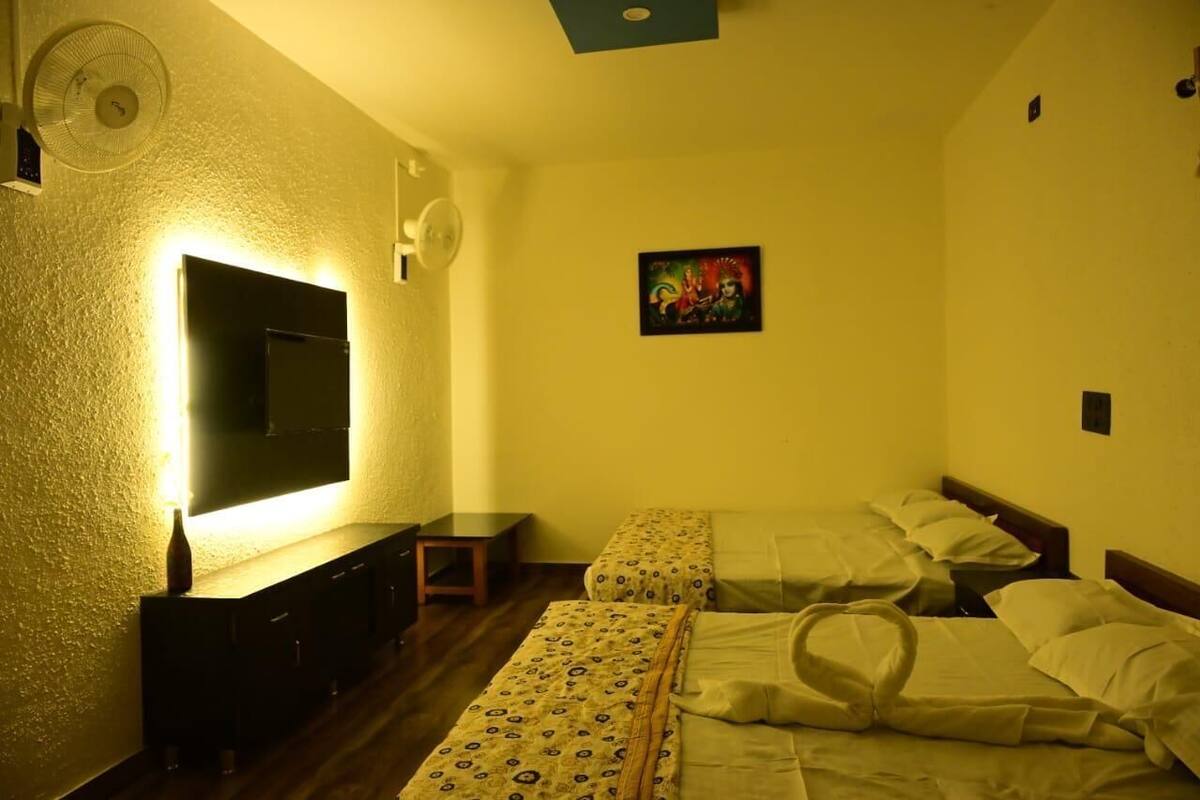 Una habitación con dos camas, un televisor montado en la pared, una mesita pequeña y un ventilador.