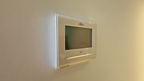 Een aan de muur bevestigde thermostaat met een beeldscherm en een aan/uit-knop.