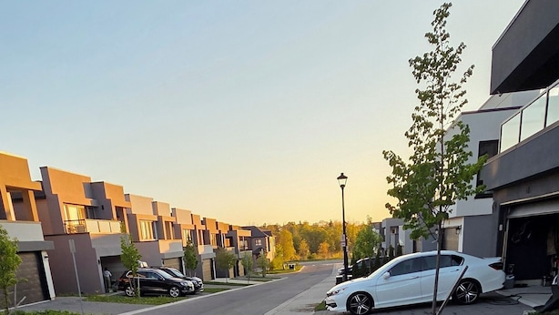 Eine moderne Wohnstraße mit gepflastertem Bürgersteig, parkenden Autos und blauem Himmel.