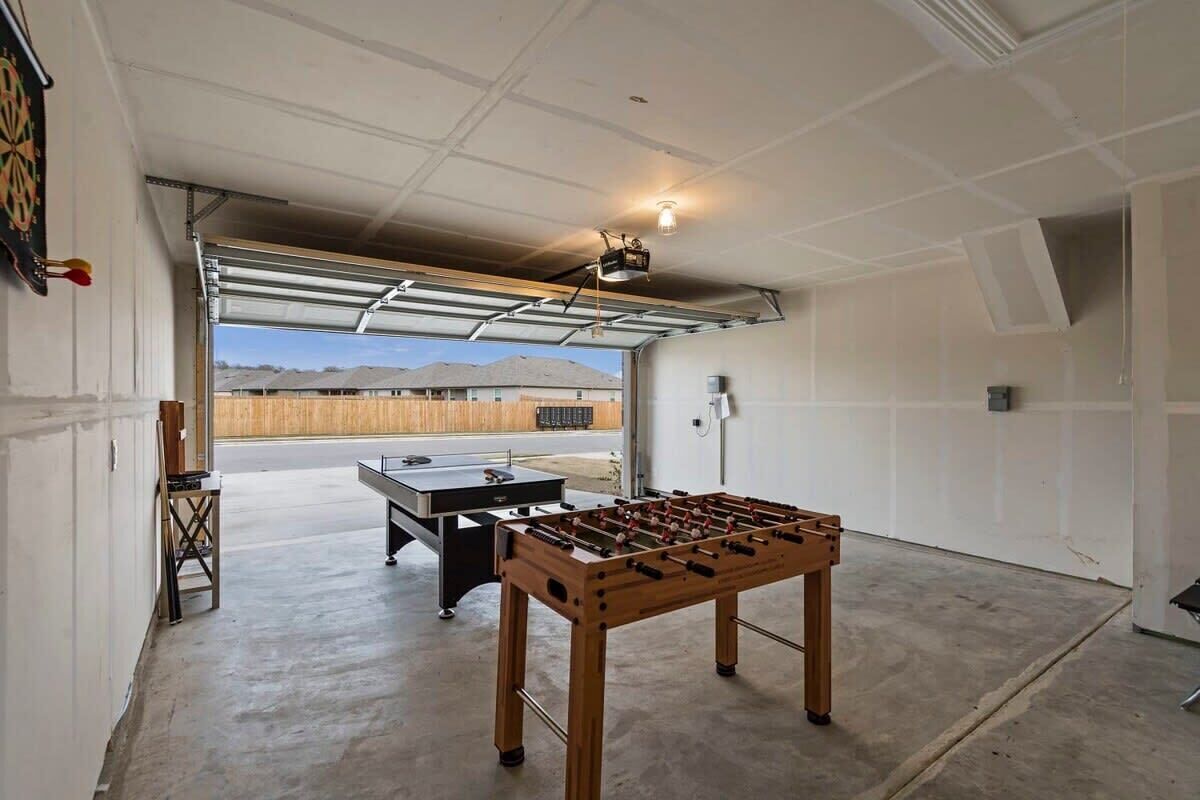 A garage with a foosball table, ping pong table, and a dartboard.