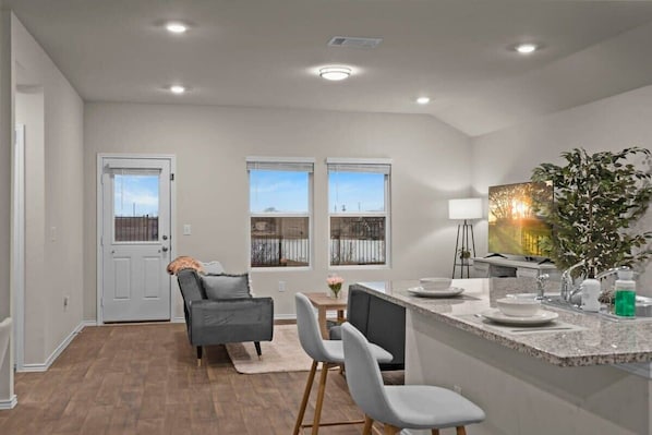 A modern kitchen with a granite countertop, a dining area with a table and chairs, and a view through the windows.