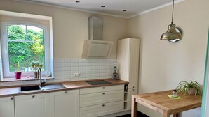 Eine Küche mit weißen Schränken, einem Fenster mit Pflanzen, einem Holztisch und einer Pendelleuchte.