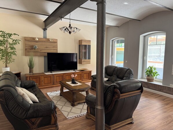 A living room with a large flat-screen TV, leather sofas, a wooden coffee table, and a chandelier. - Family-friendly, spacious vacation apartment in a quiet, rural location (Bliesdorf)