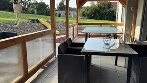 Eine Terrasse im Freien mit Tisch und Stühlen, einer gelben Rutsche und Blick auf ein grünes Feld und Bäume.