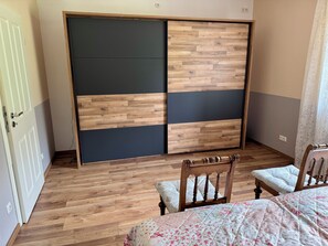 A bedroom with a wooden floor, a bed with a floral quilt, a wooden chair, and a wardrobe with a wooden and dark panel design. - Family-friendly, spacious vacation apartment in a quiet, rural location (Bliesdorf)