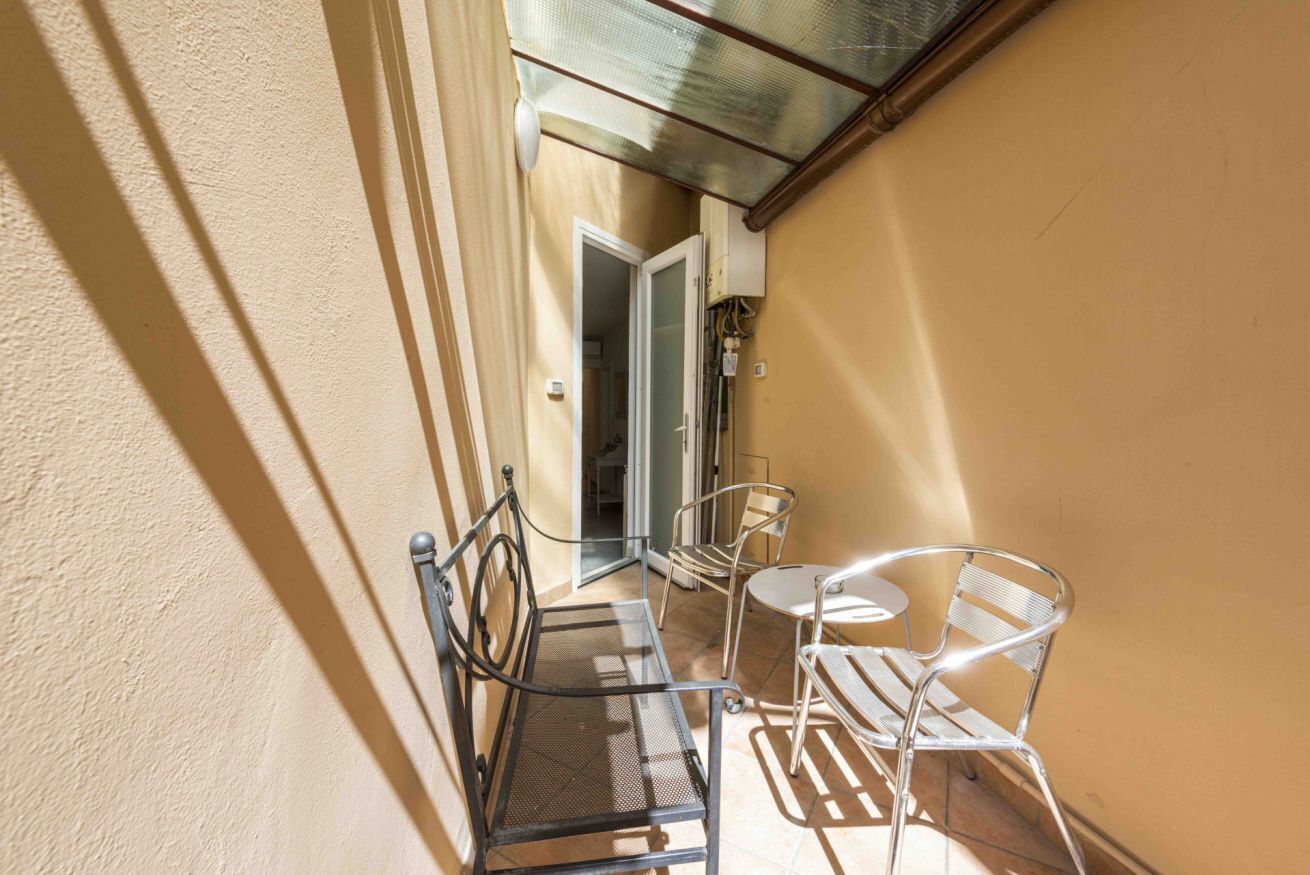 A balcony with metal chairs and a table, a door leading to an interior space, and a glass ceiling.