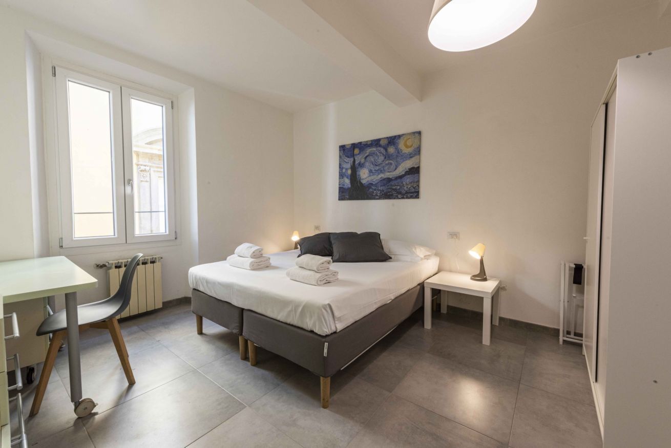 A bedroom with a bed, bedside tables, a desk, and a radiator.