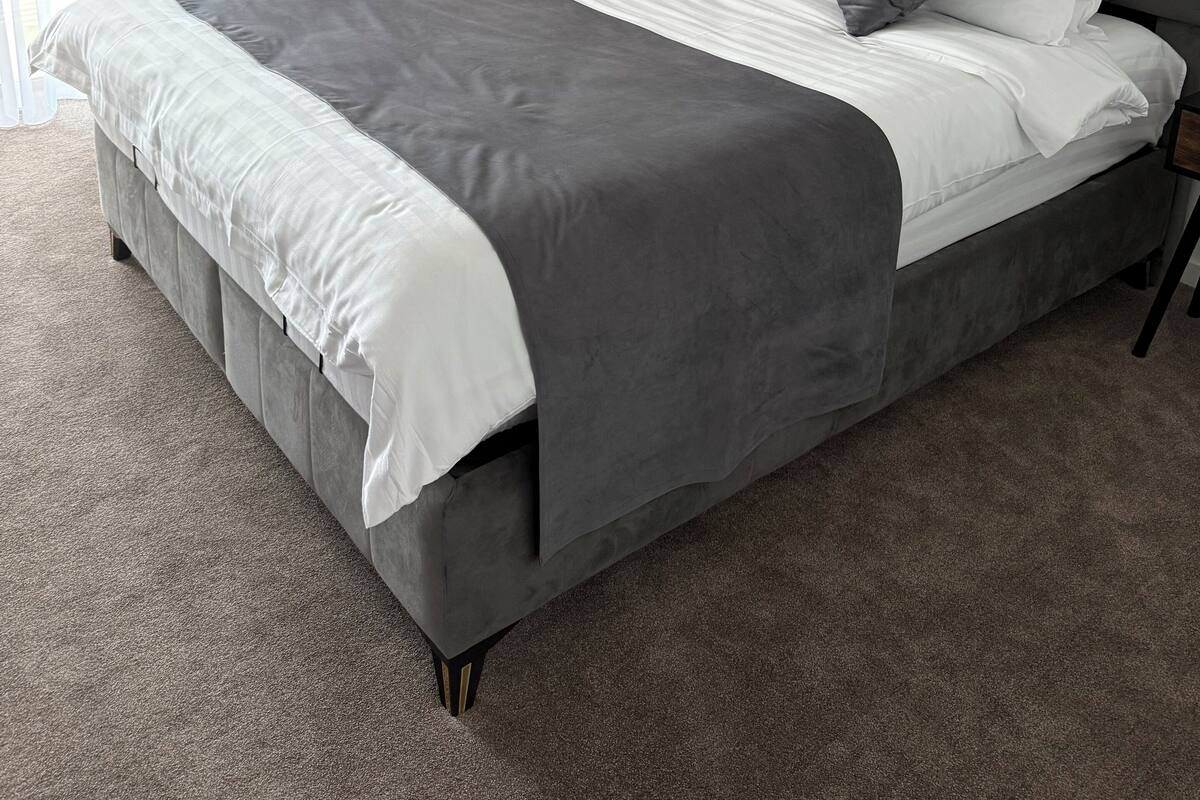 Een moderne slaapkamer met een grijs gestoffeerd bed, witte beddengoed en grijze gordijnen.