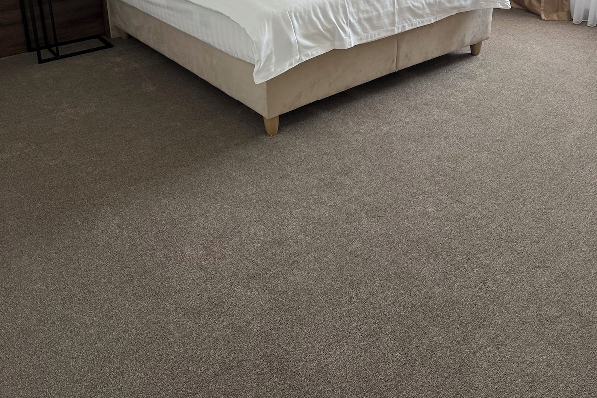 Een net opgemaakt bed met witte lakens in een hotelkamer, met een houten hoofdbord, een klein nachtkastje en een hanglamp.