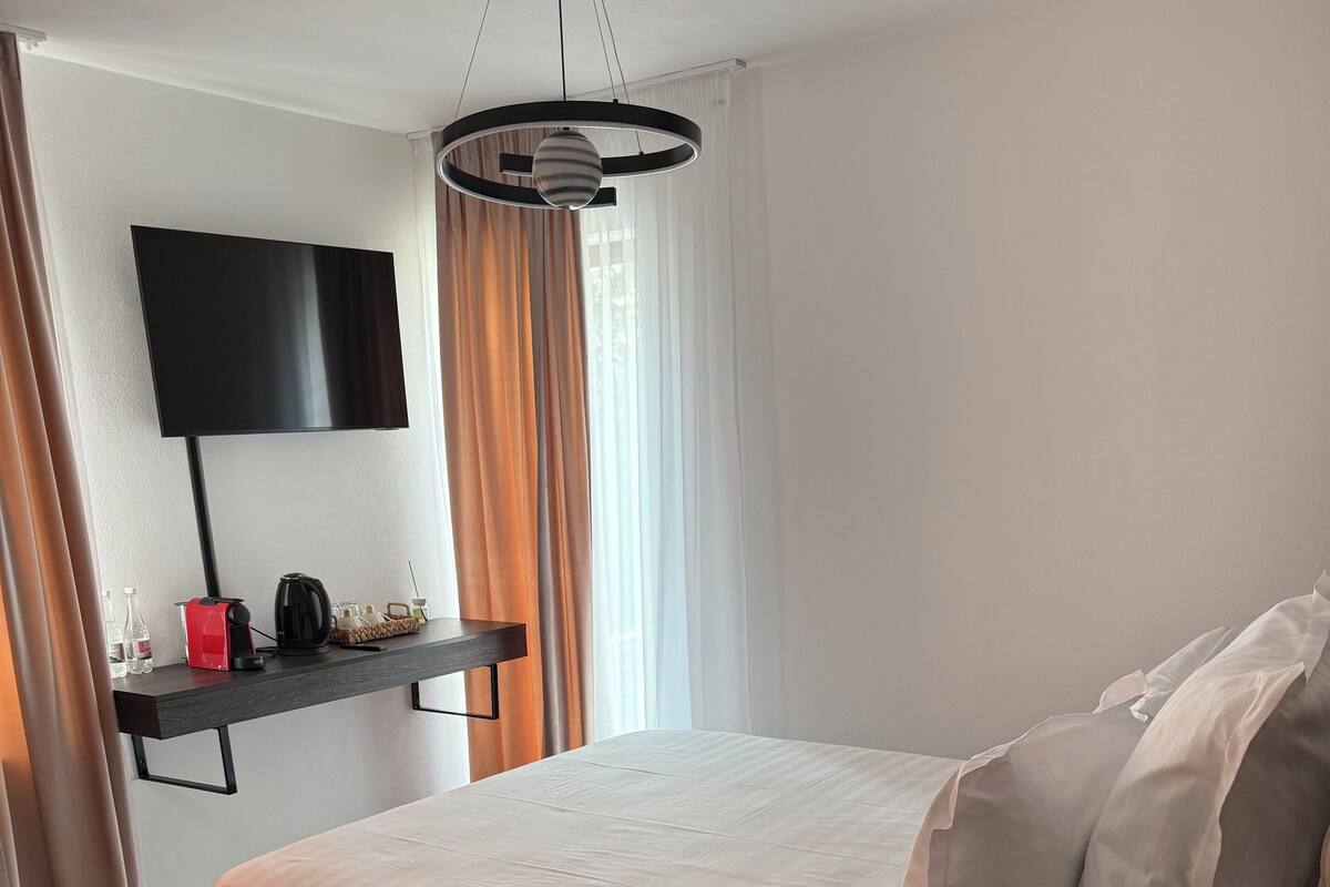 Een keurig opgemaakte slaapkamer met een bed, nachtkastje, een aan de muur bevestigde televisie en een bureau met stoel.