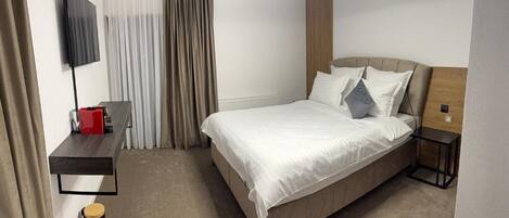 Una habitación de hotel moderna con cama, escritorio, televisor y mesita de noche.