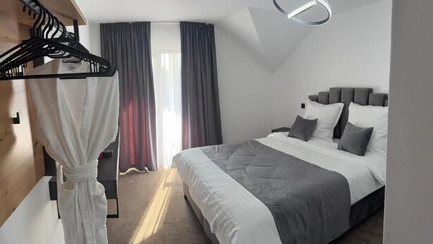 A modern hotel room with a large bed, a robe hanging on a rack, and a circular ceiling light. - Casuta de pe Ses (Novaci)