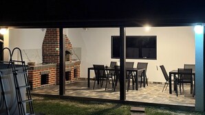 An outdoor patio with a brick barbecue, seating area, and a TV mounted on the wall. - Casuta de pe Ses (Novaci)