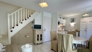 Una cocina moderna con armarios blancos, una zona de comedor con una mesa redonda y una escalera decorada con corazones.