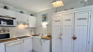 Una cocina con armarios blancos, un microondas, un lavavajillas y un fregadero. Hay tres puertas con las etiquetas 'Deauville', 'St Malo' y 'Cabourg'.
