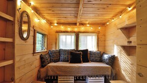 Un dormitorio acogedor tipo cabaña con cama, almohadones estampados, un espejo y luces de tipo guirnalda.