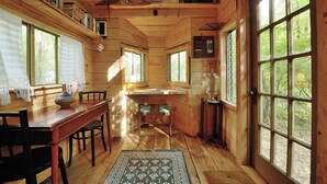 Interior de una cabaña de madera con comedor, cocina y ventanas amplias que ofrecen vistas al exterior.