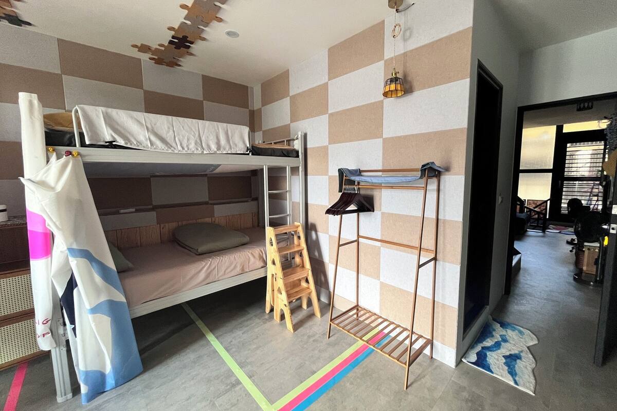 A bunk bed room with a ladder, a wooden shelf, and a colorful striped rug.