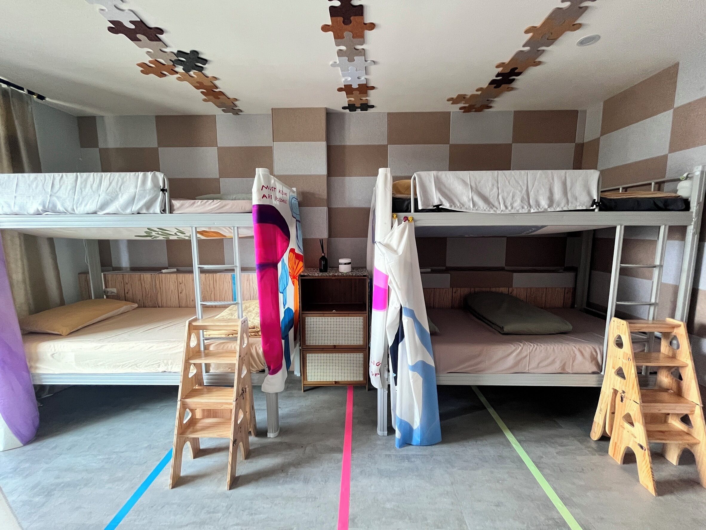 A dormitory room with two bunk beds, a desk, a chair, and a small wooden stool.