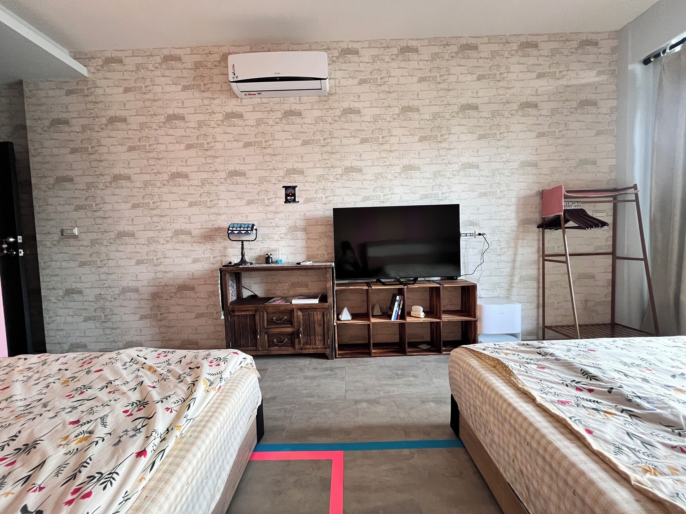 A hotel room with two beds, a TV, a brick-patterned wall, and an air conditioner.