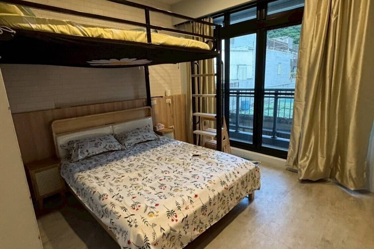 A room with a bunk bed, a large window with curtains, and a view of buildings outside.