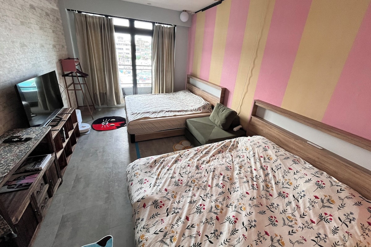 A hotel room with two beds, a TV, a desk with a computer, and a window with curtains.