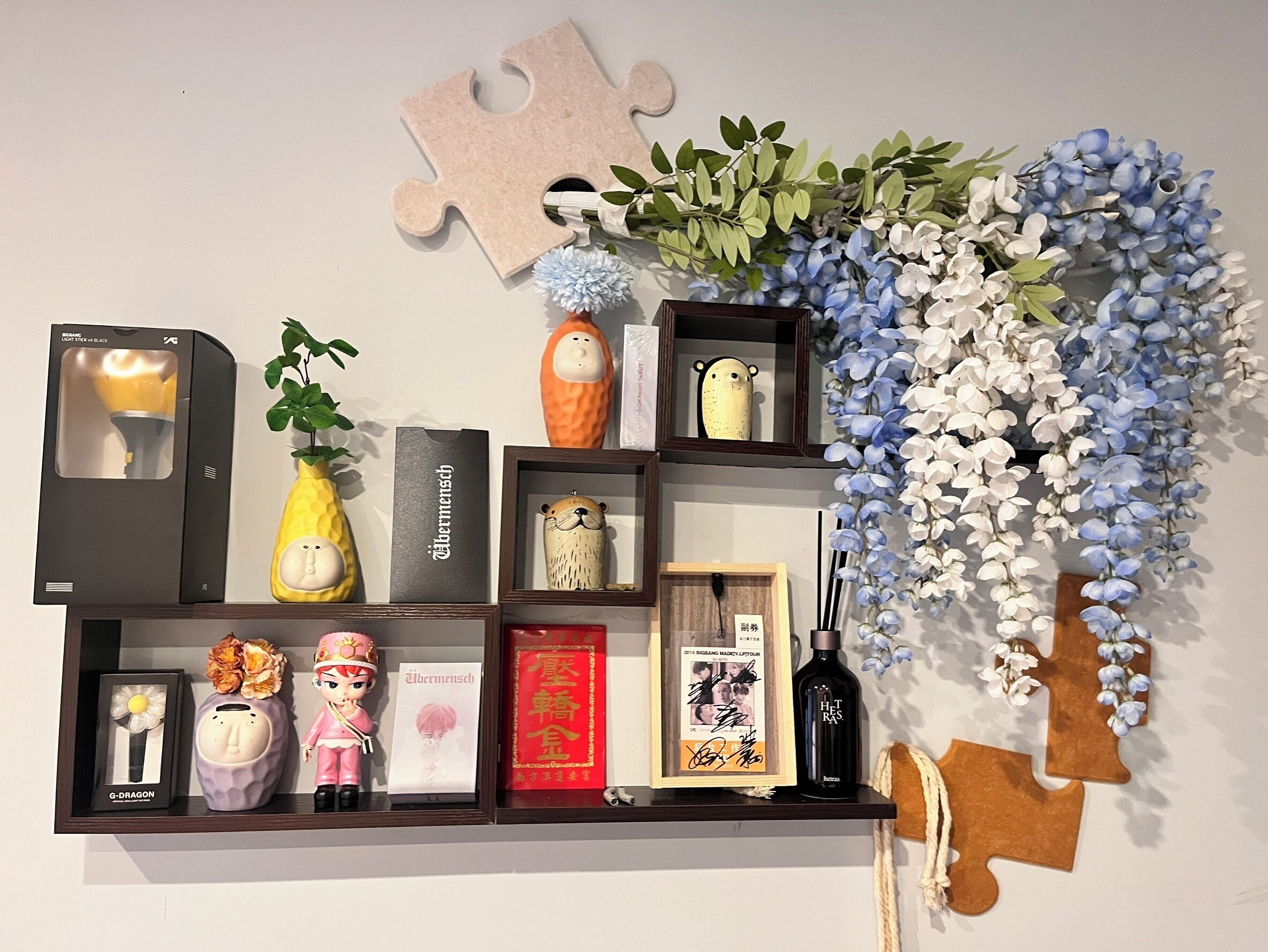 A shelf with various decorative items including a puzzle piece, artificial flowers, figurines, a framed photo, and a bottle.