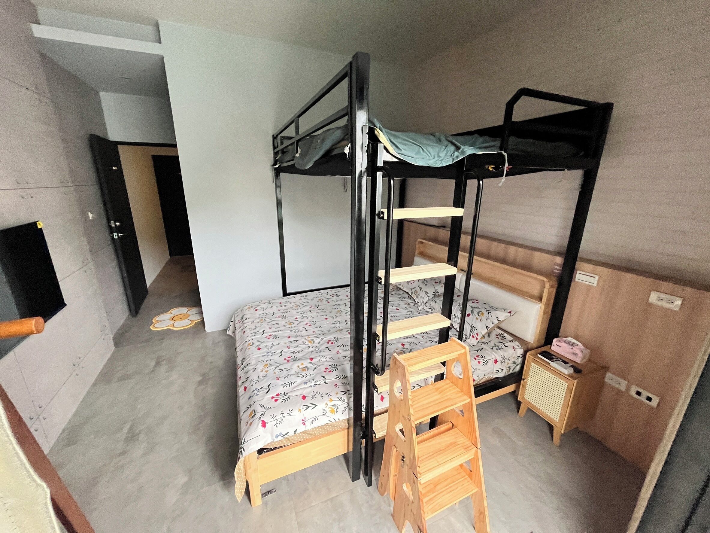A bunk bed room with a wooden ladder, a small wooden table, and a patterned bedspread.