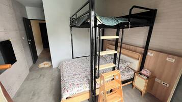A bunk bed room with a wooden ladder, a small wooden table, and a patterned bedspread.