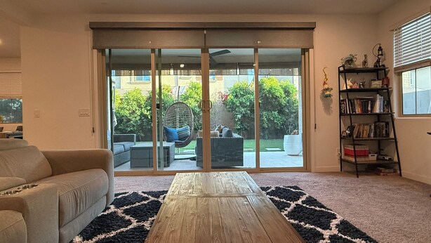 A living room with a sliding glass door leading to a patio, a beige sofa, a wooden coffee table, and a bookshelf. - Spacious 5-bedroom house with WiFi, AC in lovely Chandler (Chandler)