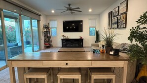 A spacious living area with a large TV, a wooden coffee table, and a clock displaying 6:05. - Spacious 5-bedroom house with WiFi, AC in lovely Chandler (Chandler)