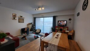 Un salon avec une table à manger en bois, des chaises rouges et noires, un sapin de Noël et un téléviseur posé sur un meuble.