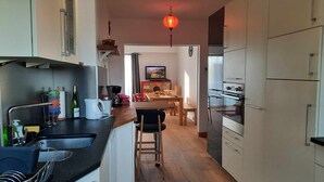 Une cuisine étroite avec un coin repas, un plancher en bois et un luminaire suspendu.