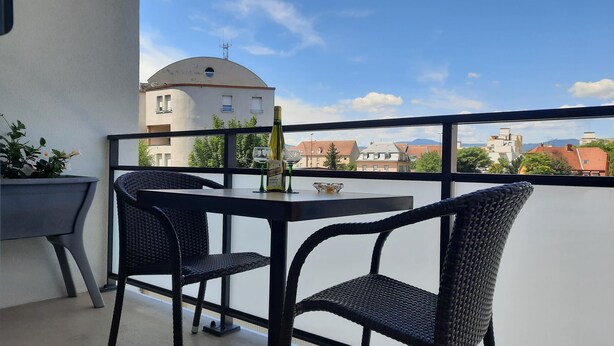 Un balcon avec une table et des chaises, une bouteille de vin et une plante en pot.