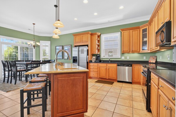 A spacious kitchen with wooden cabinets, a large island, and a dining area with chairs. - Private Pool, Gorgeous Sunsets & 10 minute walk to ALL! By Williamson Realty (Ocean Isle Beach)