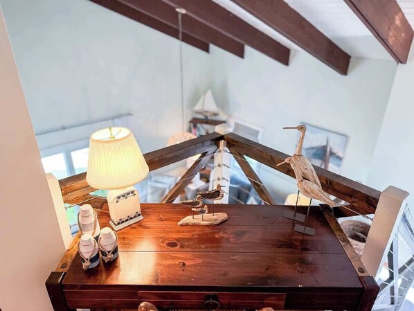 A wooden table with a lamp, decorative items, and a bird sculpture in a room with exposed beams.