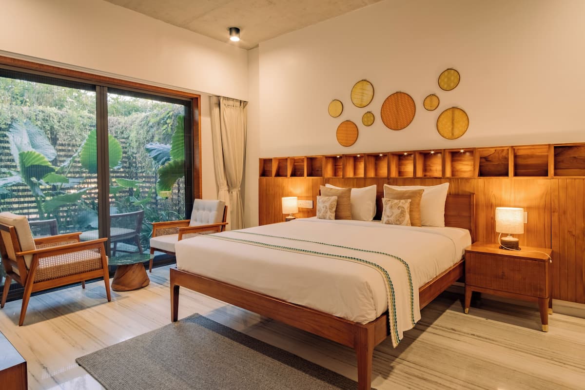 Ein geräumiges Schlafzimmer mit einem großen Bett, einem Holzkopfende und Blick auf üppiges Grün durch eine Glasschiebetür.