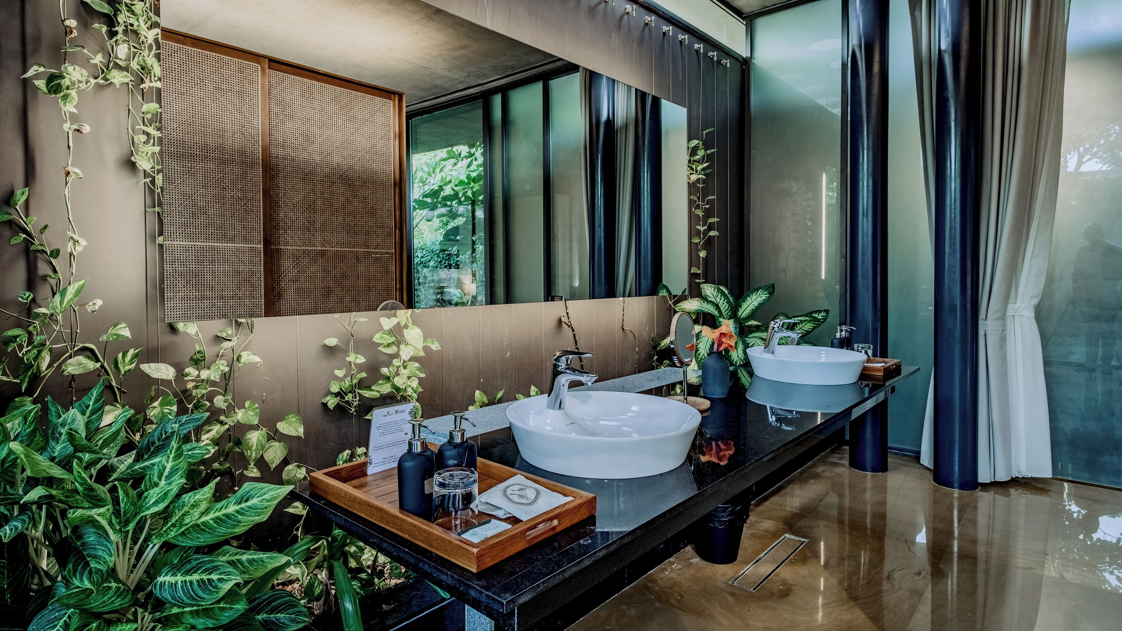 Un baño moderno con dos lavamanos, un espejo grande y plantas verdes exuberantes.